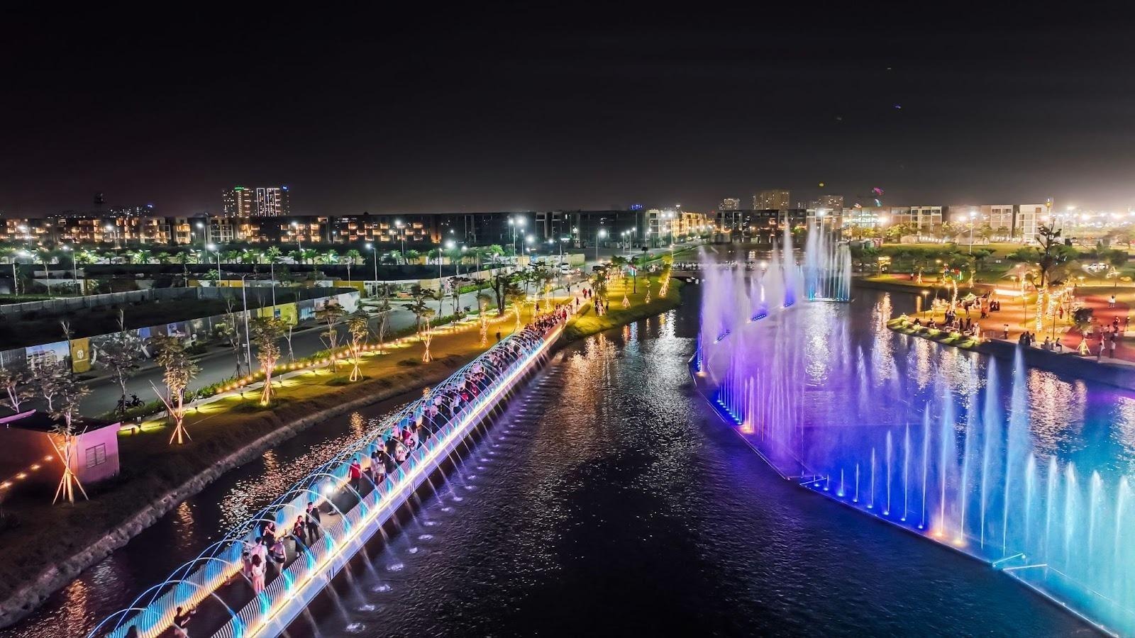 A water fountain with lights and buildings in the backgroundAI-generated content may be incorrect.